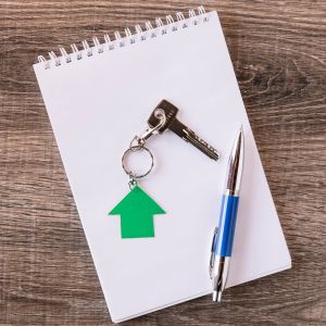 Uma chave com um chaveiro em formato de casa e uma caneta sobre um bloco de notas