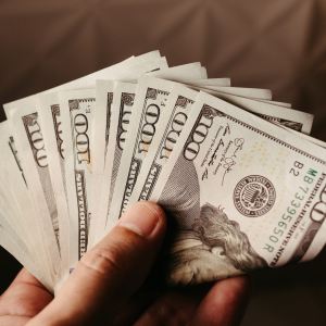 Imagem para matéria sobre vantagens e desvantagens de investir no exterior em que mostra uma mão segurando várias notas de 100 dólares.