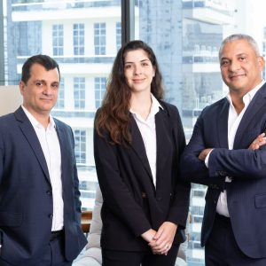 Foto de Eduardo Duarte (à esquerda), homem branco, Mariana Fenelon (ao centro, mulher branca, e Sérgio Silva (à direita), homem branco. Todos usam terno e camisa social e fazem parte da Tenax Capital