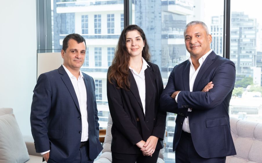 Foto de Eduardo Duarte (à esquerda), homem branco, Mariana Fenelon (ao centro, mulher branca, e Sérgio Silva (à direita), homem branco. Todos usam terno e camisa social e fazem parte da Tenax Capital