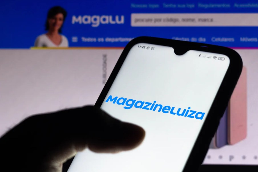Foto de uma tela de celular com o logo do Magazine Luiza (MGLU3), uma das empresas mais afetadas pela alta da Selic, taxa báscia de juros, segundo o BTG Pactual.