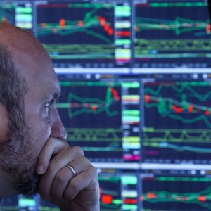 Foto de um homem olhando para cotações de telas ao fundo. A matéria lista as dez ações recomendadas que pagam dividendos para investir em janeiro de 2025.