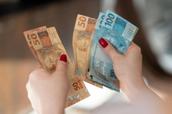 Imagem da mão de uma mulher branca contando notas de 100 reais e 50 reais.