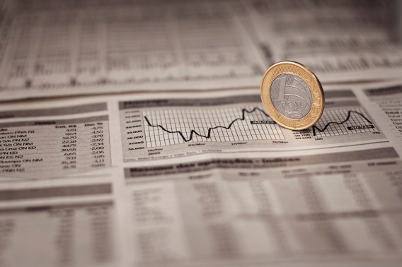 Foto de moeda de um real sobre jornal para ilustrar matéria sobre a previsão de queda da taxa Selic para 2026 segundo o banco JPMorgan