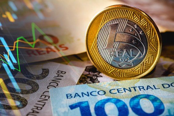 Foto de uma moeda e nota de real. A matéria descreve como investir em CDB pós-fixado hoje apresenta risco de marcação à mercado no médio e longo prazo
