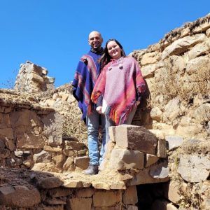 Foto de um casal em frente a uma parede de pedras. Eles vestem Ponchos coloridos.