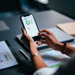 Foto de uma mão segurando um celular. Na tela, há diversos gráficos de investimentos.