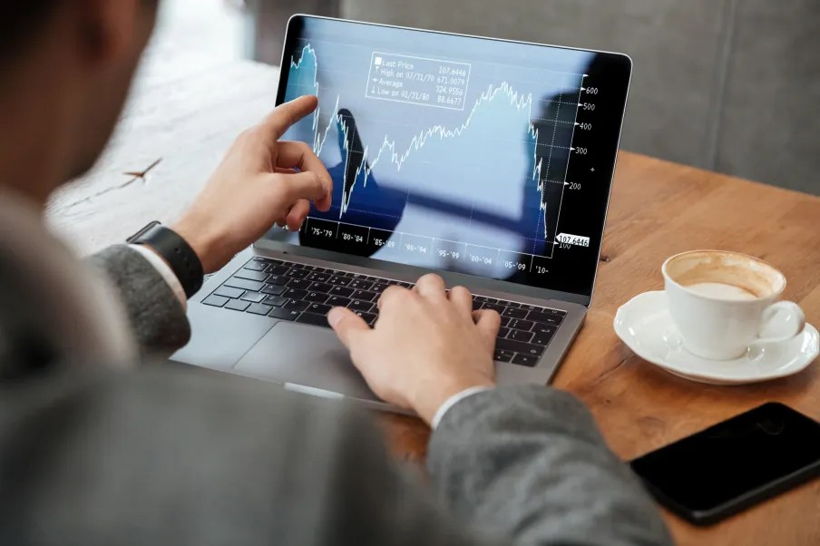 Imagem de um homem analisando um gráfico em um notebook com um café ao lado