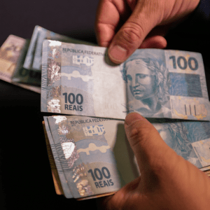 Imagem da mão de uma pessoa branca contando notas de 100 reais.